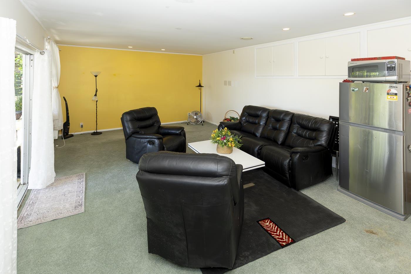 Living area before renovation: dated carpet, yellow feature wall and a fridge standing against the back wall.