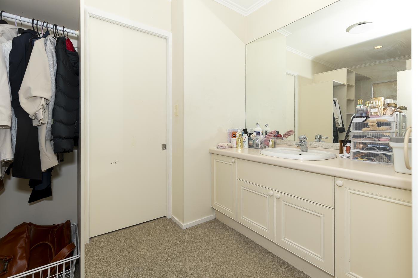 Vanity and dressing area before renovation: cream laminate cabinetry, a large mirror and carpeted floor.